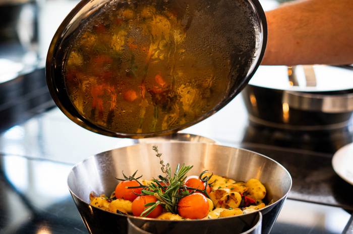 Geöffneter Topf mit Rosmarinkartoffeln und Tomaten auf dem Herd